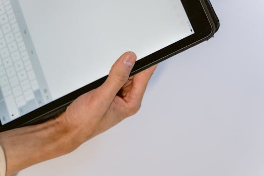 A close-up image of a hand holding a black tablet showing an open keyboard on the screen.