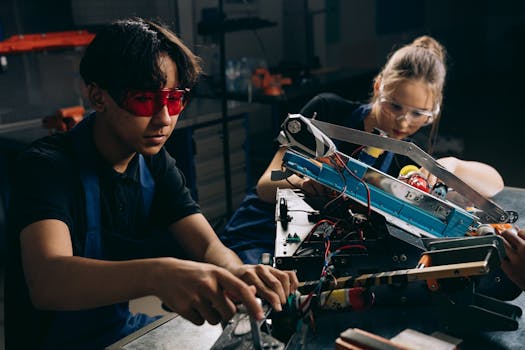 Two young engineers working on robotic equipment in a workshop setting.