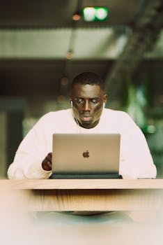 A professional focused on working at a laptop indoors, highlighting technology and concentration.